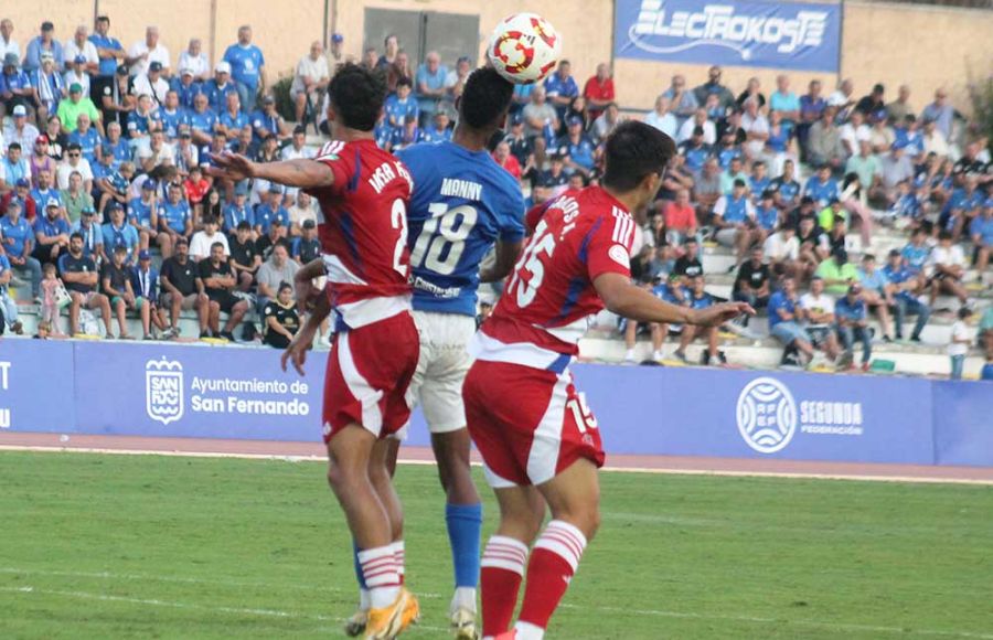 Manny Rodríguez salta con dos jugadores del Recreativo Granada durante el partido de la primera vuelta en Bahía Sur y que acabó 1-3.