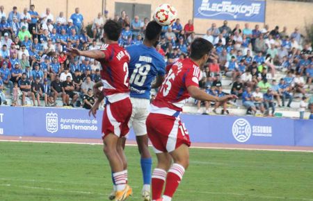 Manny Rodríguez salta con dos jugadores del Recreativo Granada durante el partido de la primera vuelta en Bahía Sur y que acabó 1-3.