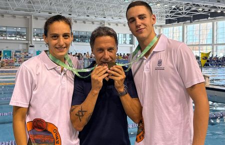 El entrenador del CN San Fernando, Pachi Arce muerde las medallas conseguidas por Irene Peinado y David Rodríguez en el Campeonato de Andalucía absoluto y junior en Málaga. 